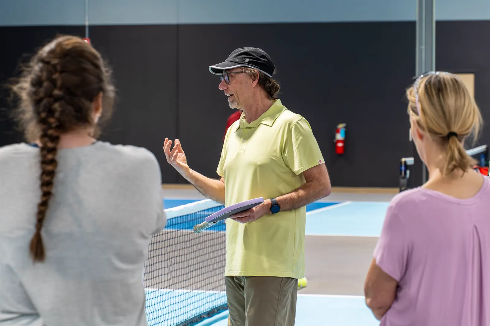 A pickleball coach explaining a drill to players near the net